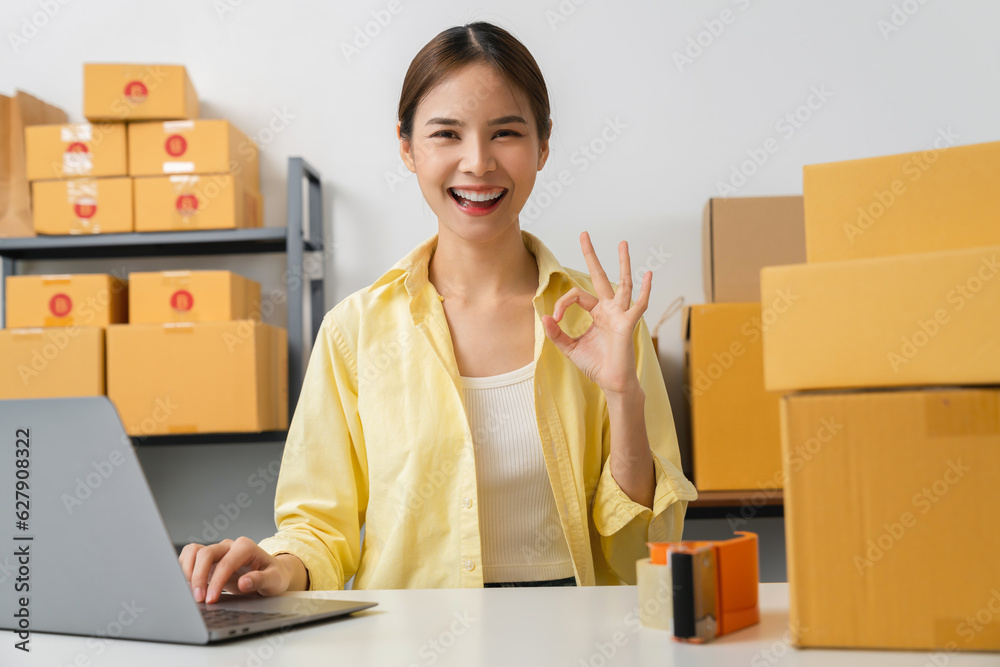 Owner holding packing carton parcel box with shows ok sign, working at the home office, seller prepares the delivery. Startup small business. Owner holding packing carton parcel box with shows ok sign, working at the home office, seller prepares the delivery. Startup small business.