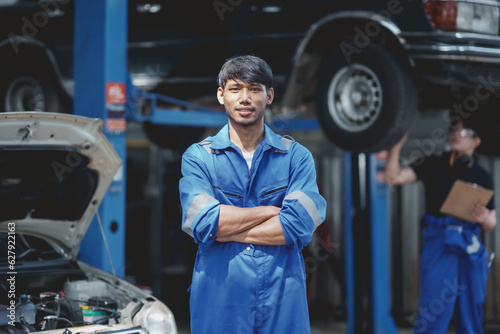 Asian man mechanic in uniform with crossed arms standing at the car repair station.