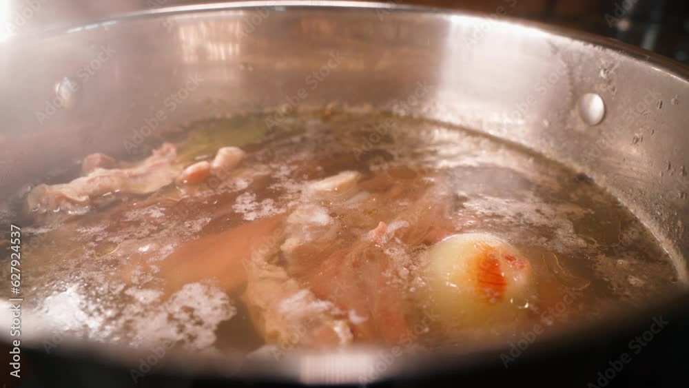 Broth with meat and onions is slowly cooked close-up. Hearty meat broth in a large steaming pot Broth with meat and onions is slowly cooked close-up. Hearty meat broth in a large steaming pot