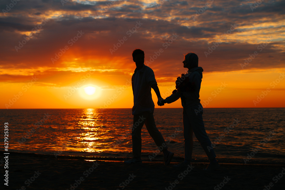 Romance, sunset date. Silhouette of guy and girlfriend holding hands together walking along shore by sea, young couple in love