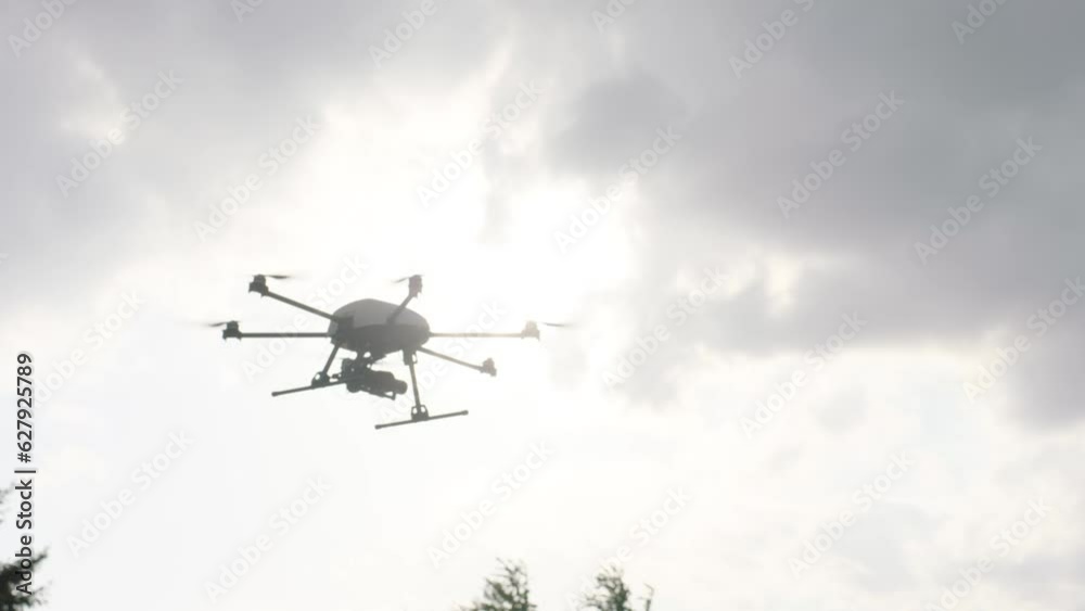 Handheld camera tracks a white drone with six propellers, flying towards the right in a cloudy sky with the sun peeping through Handheld camera tracks a white drone with six propellers, flying towards the right in a cloudy sky with the sun peeping through
