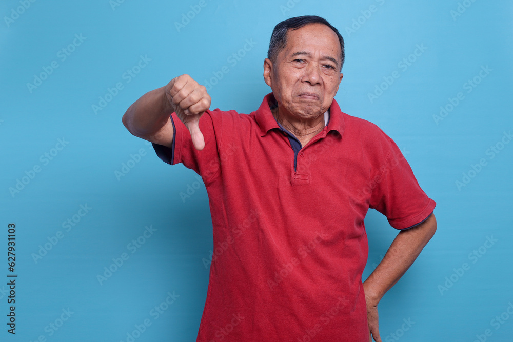 Elderly man showing thumb down dislike gesture isolated on blue background. People lifestyle concept Elderly man showing thumb down dislike gesture isolated on blue background. People lifestyle concept