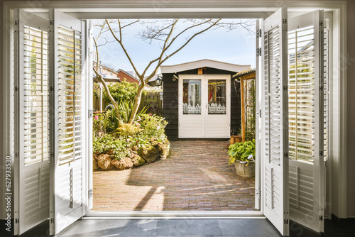 Fotografía an open front door with shutters on the outside and trees in the yard behind it,