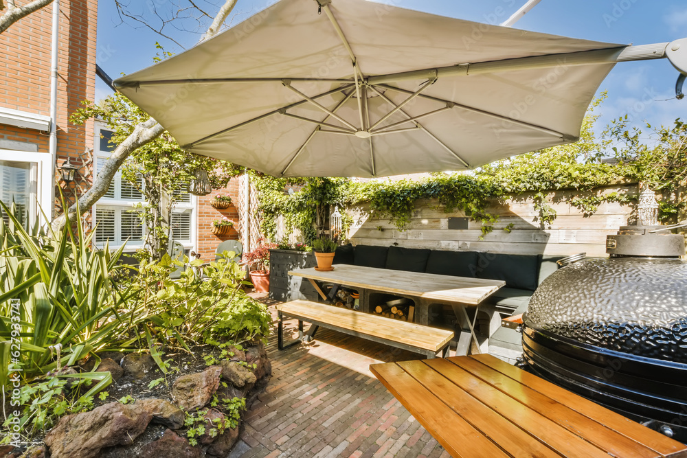 a patio with an umbrella over the table and grill in the back yard, on a sunny day photo taken from behind