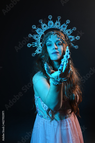 portrait of beautiful brunette woman wearing ornate silver crown headdress, posing with arm gestures, conjuring magical spell. isolated on dark studio background, cinematic blue moonlight lighting.