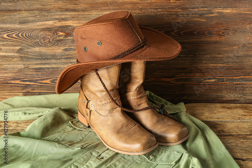 Cowboy boots, hat and shirt on wooden background