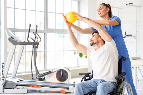 Female physiotherapist working with young man in wheelchair at rehabilitation center