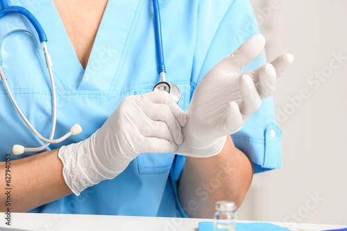 Female doctor putting on medical gloves in clinic, closeup