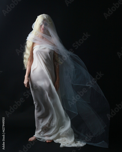 фотографія Full length portrait of beautiful blonde woman wearing white gown dress with flowing ghostly veiled fabric, isolated on dar studio background