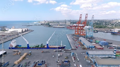 Cargo ship with tall cranes and containers in background at Haina port in Santo Domingo, Dominican Republic. Aerial drone view photo