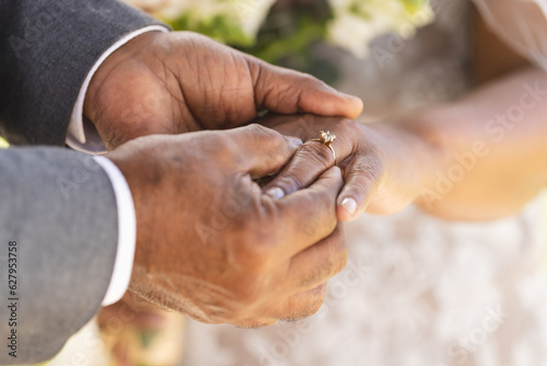 Hands of senior biracial groom putting wedding ring on finger of his bride