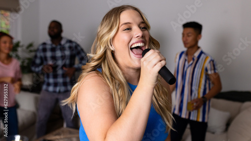 Happy diverse friends dancing and karaoke singing with microphone at home