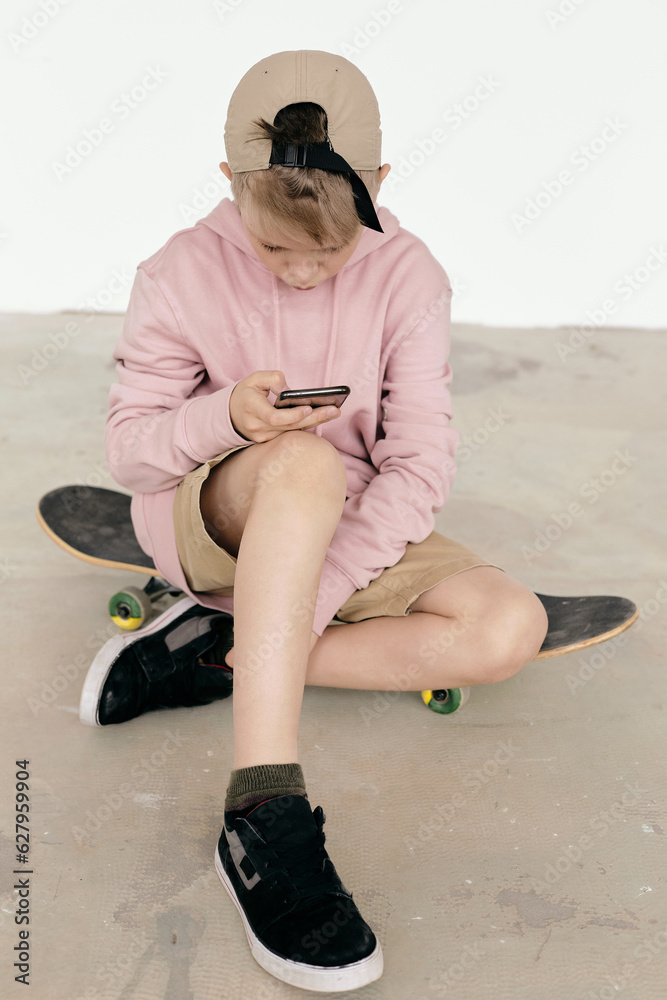 Full shot of young boy sitting on skateboard chatting on his smartphone Full shot of young boy sitting on skateboard chatting on his smartphone