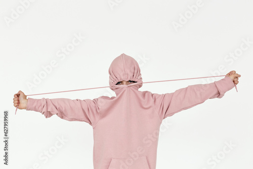 Waist-up shot of boy wearing powder pink hoodie hiding his face against white background photo