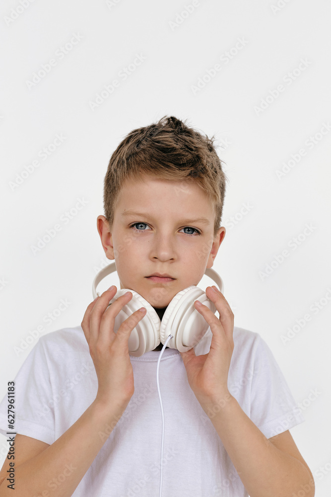 Portrait of preteen boy wearing white T-shirt touching his headphones and looking at camera Portrait of preteen boy wearing white T-shirt touching his headphones and looking at camera