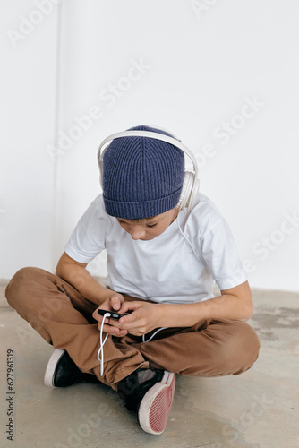 Vertical shot of preteen boy sitting on floor with crossed legs and choosing audio track to listen to