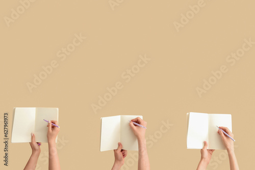 Hands writing in open notebooks on beige background