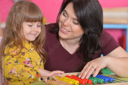 Young woman teaches a little girl math on wooden abacus. The girl is learning to count. Mom helps her.