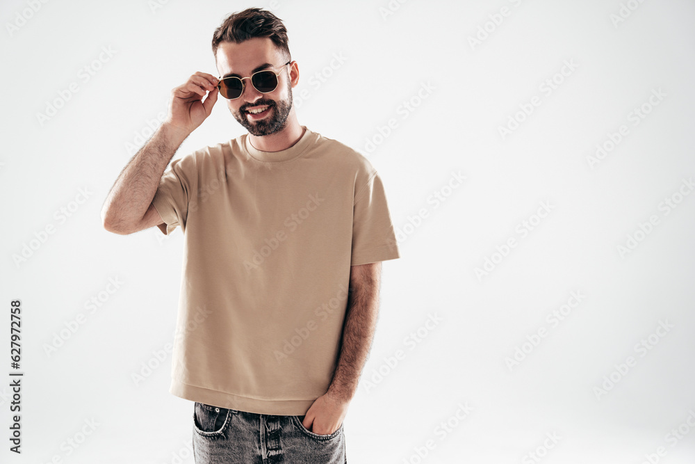 Fototapeta premium Portrait of handsome smiling stylish hipster lambersexual model. Sexy man dressed in T-shirt and jeans. Fashion male isolated on white background in studio. In sunglasses