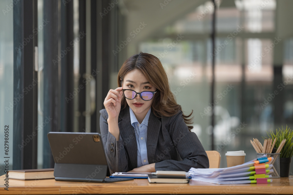 An Asian businesswoman sitting at a desk and looking through glasses at the camera.