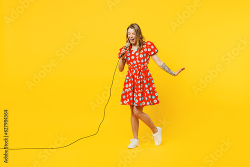 Full body excited happy cheerful young caucasian woman she wear red dress casual clothes sing song in microphone at karaoke club isolated on plain yellow background studio portrait. Lifestyle concept.