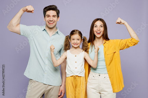 Young happy parents mom dad with child kid daughter girl 6 years old in blue yellow casual clothes show hand biceps muscles demonstrating power isolated on plain purple background. Family day concept.