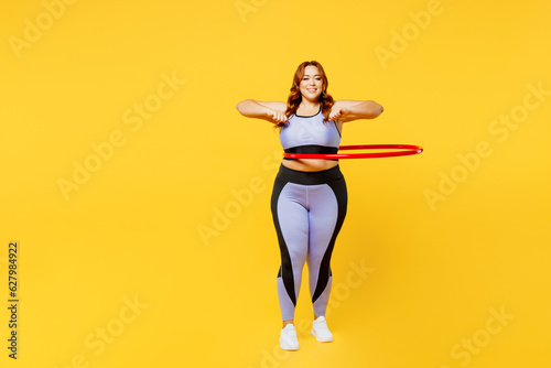 Full body young fun chubby plus size big fat fit woman wear blue top warm up training using hula hoop for waist weight loss isolated on plain yellow background studio home gym. Workout sport concept.