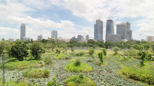 Benchakitti Park in Bangkok. Nearby, the skyscrapers of the business district are visible. A place of relaxation for residents, with a path around green areas. Skyscrapers, Urban park, Cityscape. photo