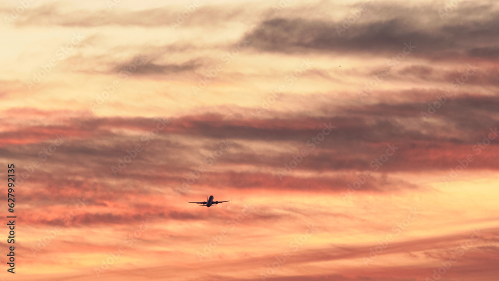 Fototapeta premium Airplane flying across a vibrant sunset sky with colorful clouds in the evening hours over a scenic landscape