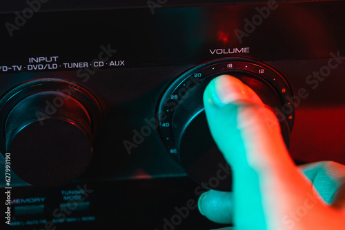 A woman's hand turns on and increases the volume of music on the amplifier. Colorful neon light. Macro view. Close-up of volume controls panel. Audio Receiver Control Panel. Control panel by sound amp photo