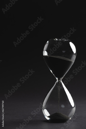 Close up of hourglass with black sand and copy space on black background