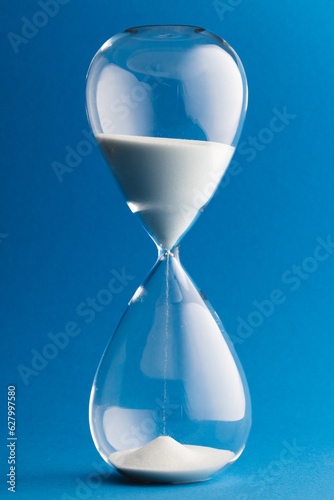 Close up of hourglass with white sand and copy space on blue background