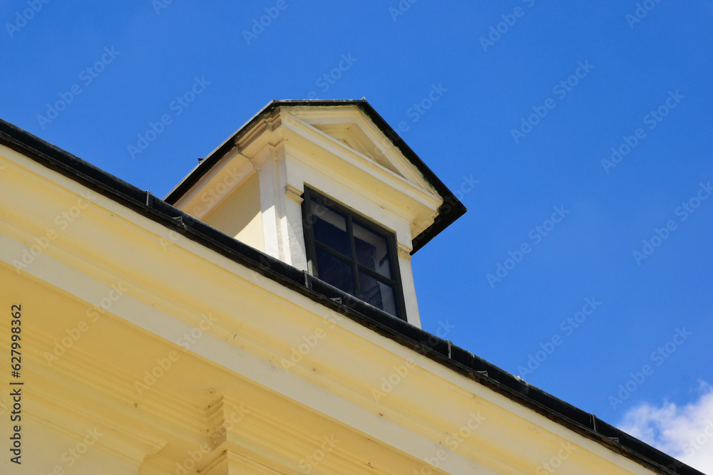 Sloped clay tile roof edge with tin gutter. old stucco roof dormer with small wood window. classic old european residential building construction style.