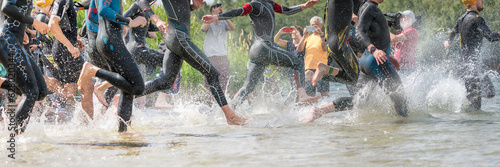Fotografie Athletes in wetsuits running into a lake at a triathlon competition