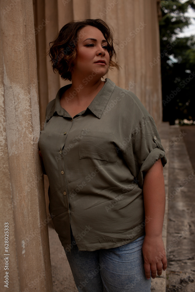 A beautiful girl is wearing a khaki t-shirt and jeans, the overweight woman posing against stone biege wall. The fashion outfit for plus-size woman for the city, minimalizm urban style clothes A beautiful girl is wearing a khaki t-shirt and jeans, the overweight woman posing against stone biege wall. The fashion outfit for plus-size woman for the city, minimalizm urban style clothes
