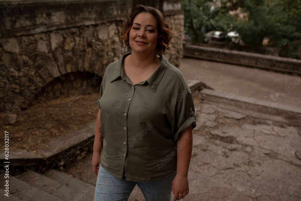Portraiy of a beautiful girl is wearing a khaki t-shirt, the overweight woman posing against stone biege wall. The fashion outfit for plus-size woman for the city, minimalizm urban style clothes Portraiy of a beautiful girl is wearing a khaki t-shirt, the overweight woman posing against stone biege wall. The fashion outfit for plus-size woman for the city, minimalizm urban style clothes