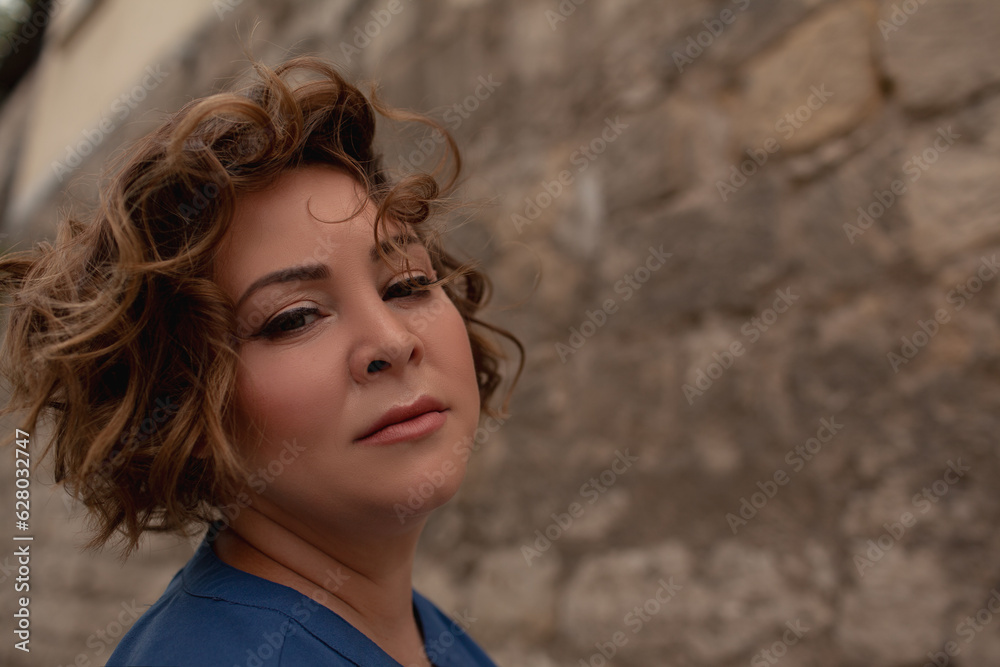 portrait of a beautiful girl is wearing a blue t-shirt, the overweight woman posing against stone biege wall. The fashion outfit for plus-size woman for the city, minimalizm urban style clothes portrait of a beautiful girl is wearing a blue t-shirt, the overweight woman posing against stone biege wall. The fashion outfit for plus-size woman for the city, minimalizm urban style clothes