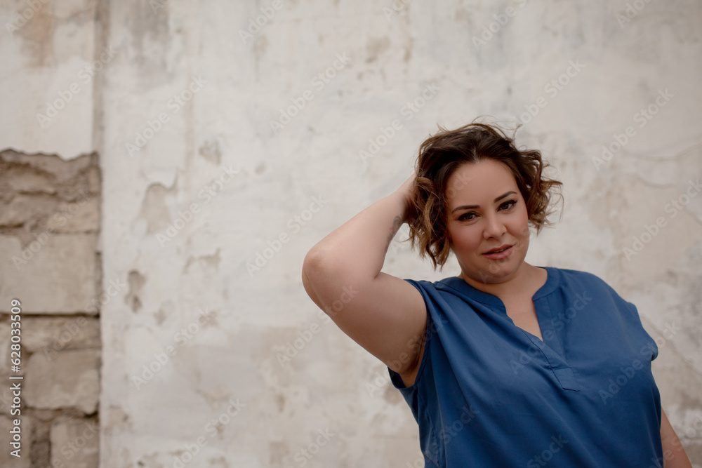 A beautiful girl is wearing a blue t-shirt and jeans, the overweight woman posing against stone biege wall. The fashion outfit for plus-size woman for the city, minimalizm urban style clothes A beautiful girl is wearing a blue t-shirt and jeans, the overweight woman posing against stone biege wall. The fashion outfit for plus-size woman for the city, minimalizm urban style clothes
