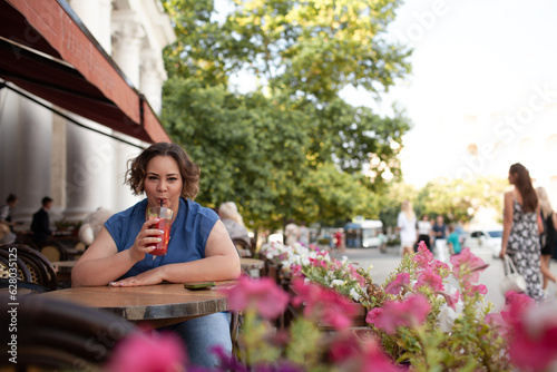 Beautiful young woman sit in cafe with glass of cooly drink. Plus size woman drink red juice and smiling