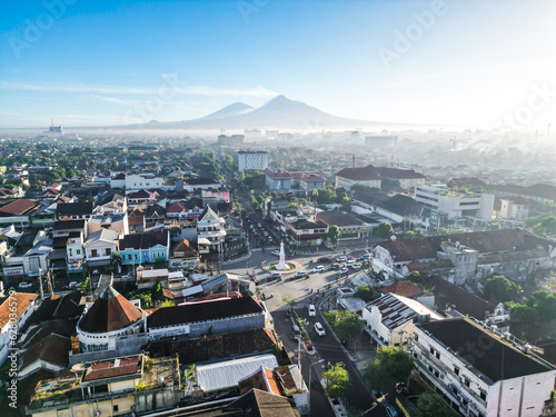 Aerial view of Yogyakarta city and Tugu Jogja Monument with lots buildings overlay and crowded vehicles traffic in the morning sunlight. Bird view of Jogjakarta with clear blue sky and merapi mountain photo
