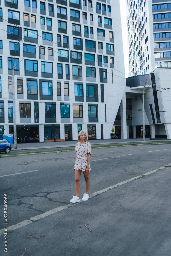 a beautiful girl walks around the city among houses and cars, in a pink dress and white sneakers a beautiful girl walks around the city among houses and cars, in a pink dress and white sneakers