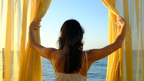 adult woman opening curtain to look at sea view