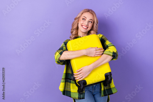 Photo of cute dreamy lady wear plaid yellow shirt hugging suitcase looking empty space isolated violet color background