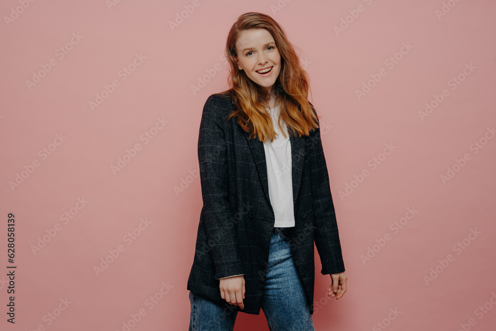 Stylish young woman in plaid blazer and jeans, posing carefree and expressing positive emotions in studio, isolated on pink wall background. Happy people concept. Stylish young woman in plaid blazer and jeans, posing carefree and expressing positive emotions in studio, isolated on pink wall background. Happy people concept.