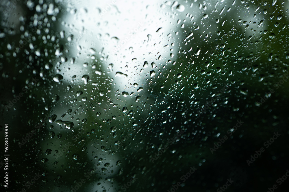 Rain water droplets accumulating on a car's window glass. Close up shot, shallow depth of field, no people, selective focus