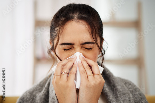 Tissue, nose and sick woman sneezing in living room with allergy, cold or flu in her home. Hay fever, sinusitis and female with viral infection, risk or health crisis in lounge with congestion photo