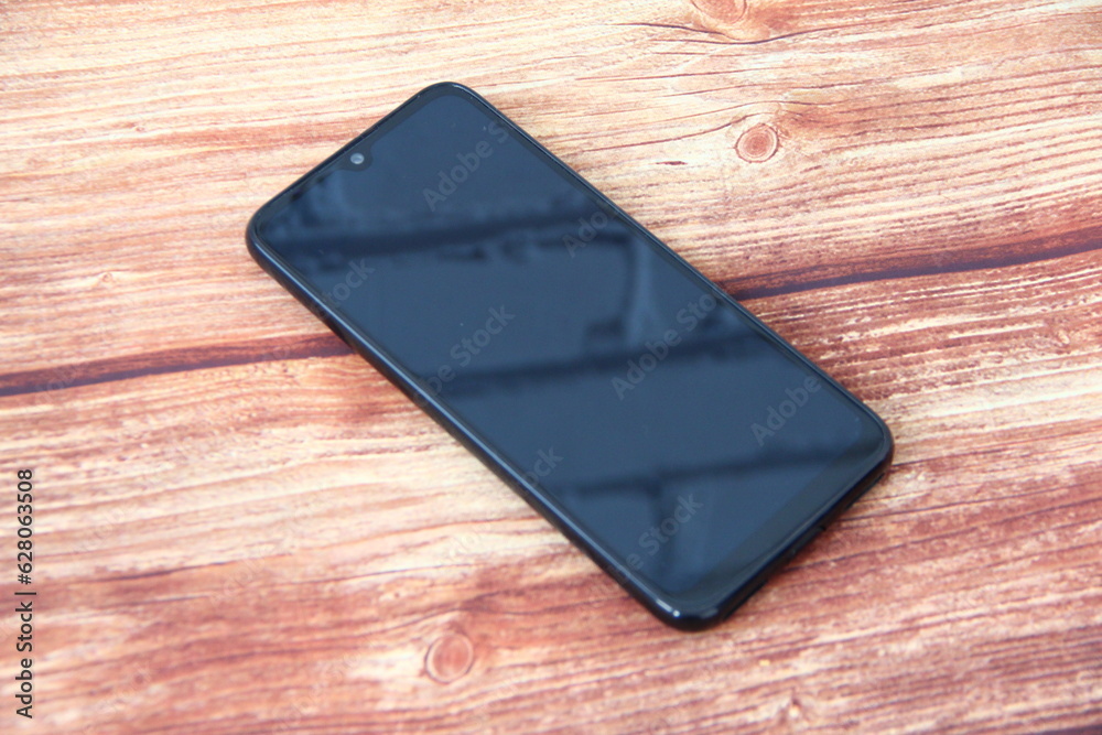 Smartphone with a black screen in which a brick wall is reflected on the wooden background Smartphone with a black screen in which a brick wall is reflected on the wooden background