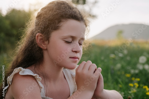 Close up of pretty little girl kid sitting in grass praying alone during sunset, child prayer, World Day of Prayer, international day of prayer, trust concept, hope, gratitude, thankful, trust