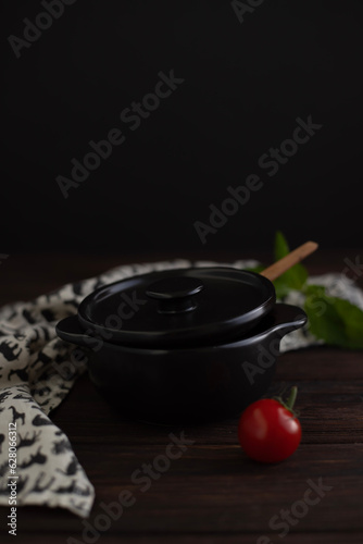 Black heat-resistant pot for baking  tomato on a dark background. Dinner
