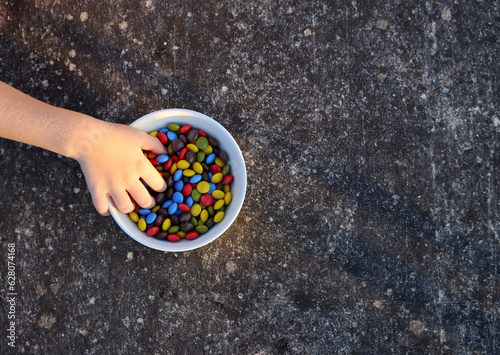 Child's hand in a bowl with round multi-colored candies.
